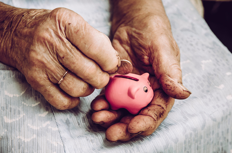 Hands of elderly putting money into piggy bank